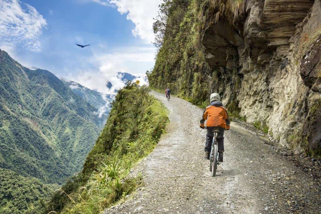 Bike adventure travel photo. Bike tourists ride on the road of death downhill track in Bolivia. In the background sky circles a condor over the scene