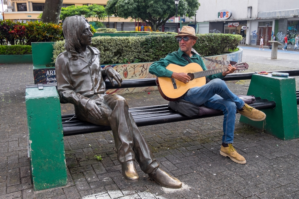 Man-playing-a-guitar-next-to-the-John-Lennon-statue-in-the-urban-city-center