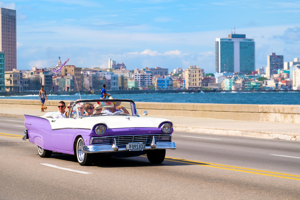  Tourists enjoying a ride on a classic american convertible car at the famous seaside Malecon avenue in Havana