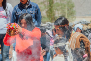 A woman raises an offering vessel in front of the fire at the ceremony of assumption of the new cacique of the colla community of Antofalla