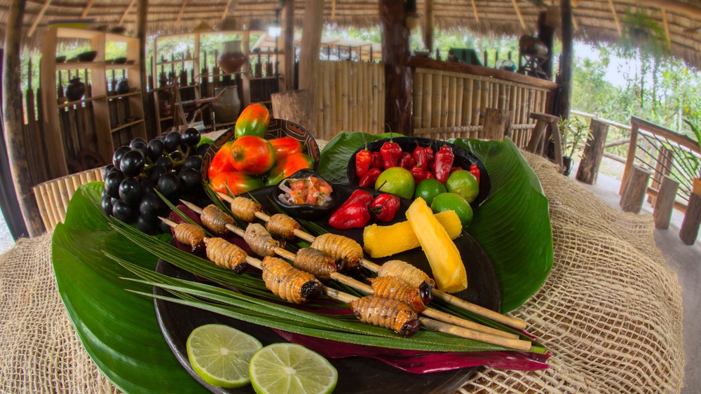 Chontacuros or Mayones (roasted worms) worms on a clay plate accompanied with lemon, chontaduros and yucca on green leaves