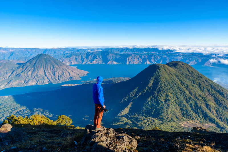 Hiker-with-panorama-view-of-Lake-Atitlan-and-volcano-San-Pedro-and-Toliman-early-in-the-morning-from-peak-of-volcano-Atitlan-Guatemala.