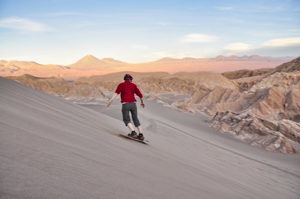 Sandboarding-during-sunset-in-Atacama-desert-chile.-A-guy-on-a-snowboard-riding-down-a-dune.-Sandboarding-in-the-Valle-de-la-Luna